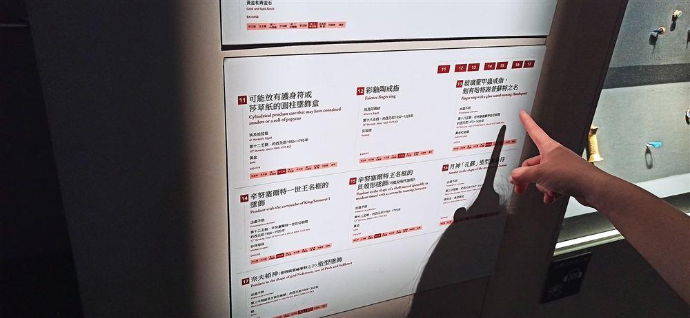 珠寶群組說明牌(11–17):圓柱墜飾盒、哈特謝普蘇特玻璃聖甲蟲戒指、月神孔蘇護身符等。