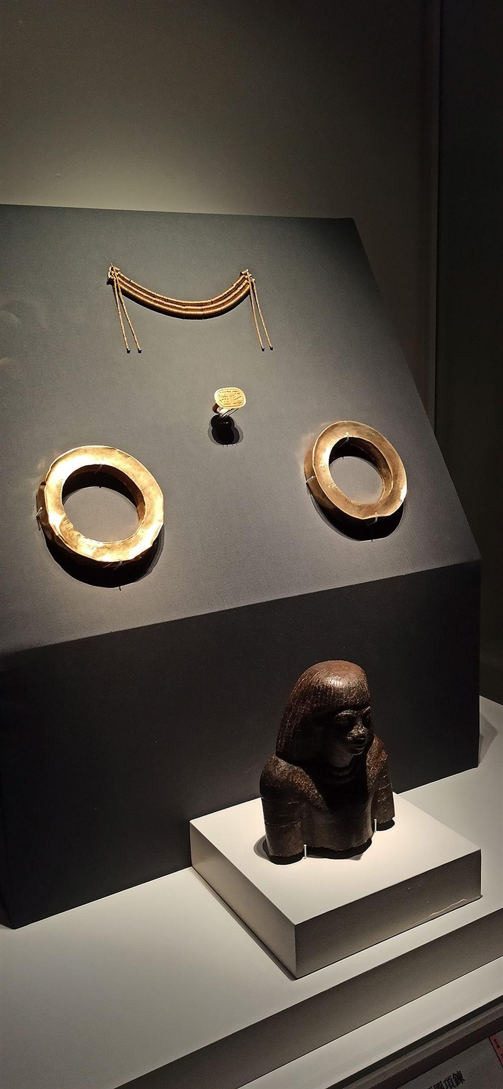 展櫃:金屬絲項鍊、金戒指、黃金手鐲與女性半身像。